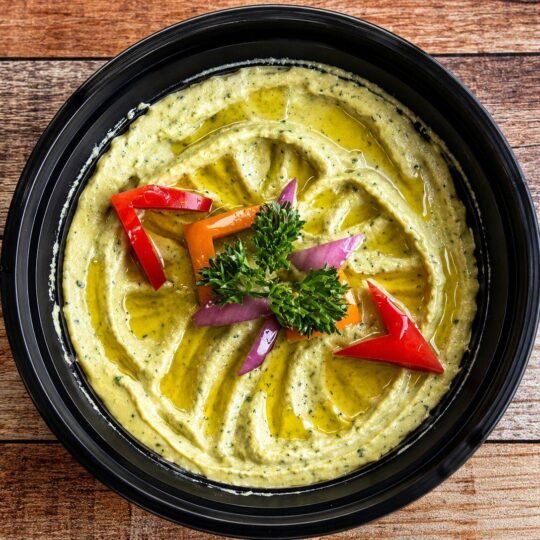 Avocado hummus topped with peppers, red onion and olive oil